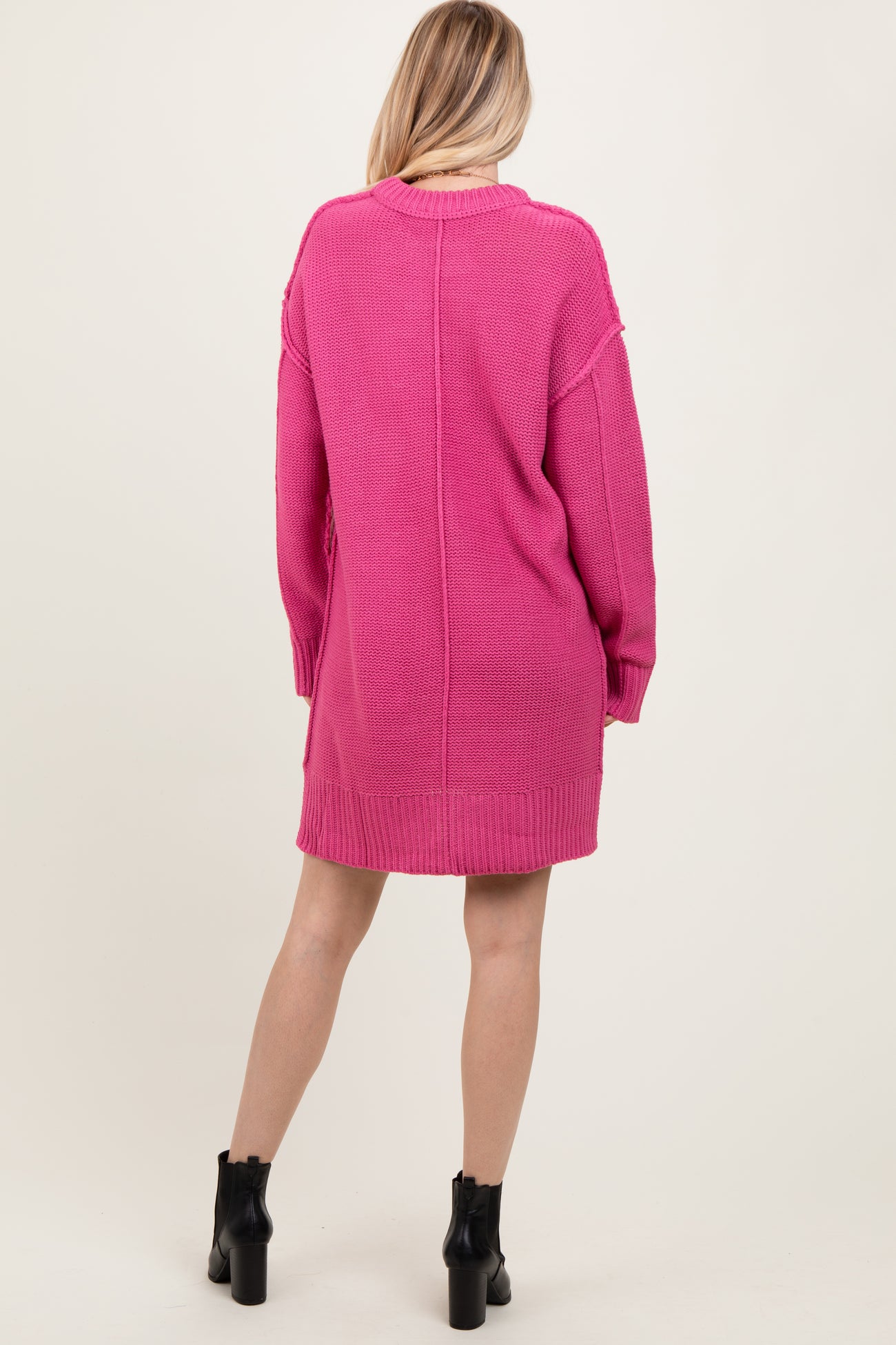woman wearing a bright pink oversized knitted sweater dress with long sleeves and a relaxed fit, viewed from the back