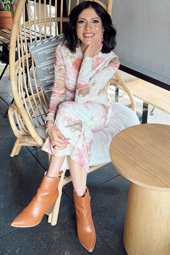 woman wearing a floral long-sleeve midi dress and brown pointed ankle boots sitting in a chair