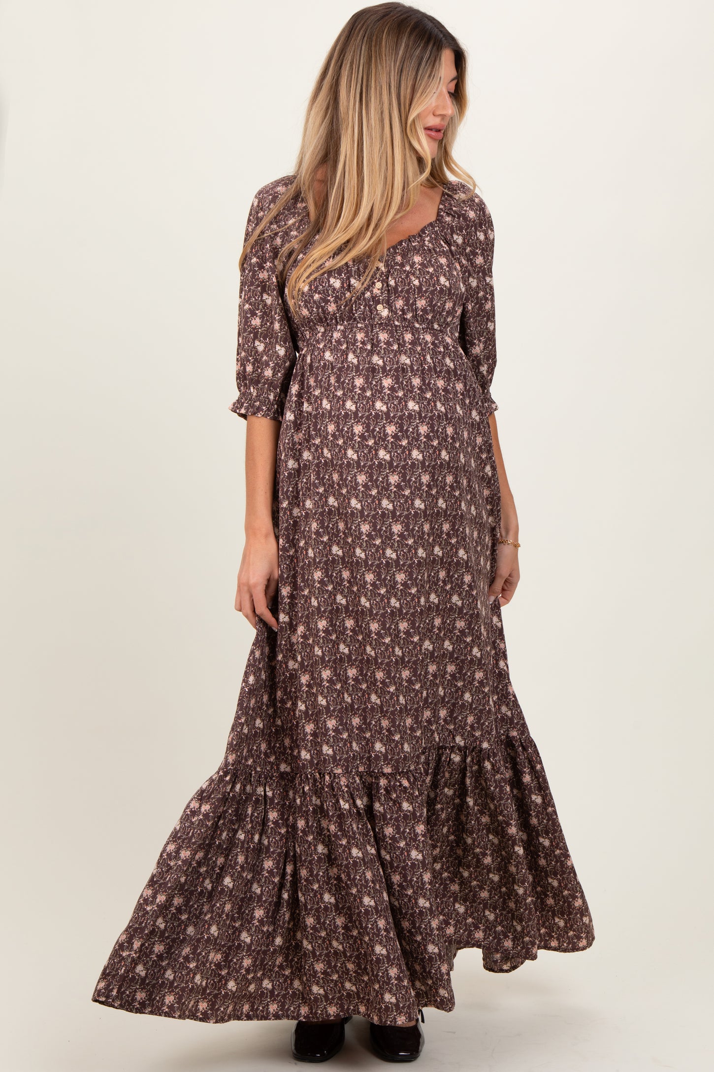 woman wearing a brown floral maternity maxi dress with puff sleeves and a tiered skirt, showing her baby bump