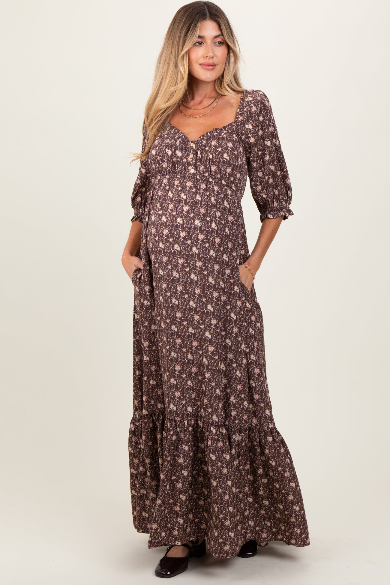woman wearing a brown floral maternity maxi dress with puff sleeves and pockets, showcasing her baby bump