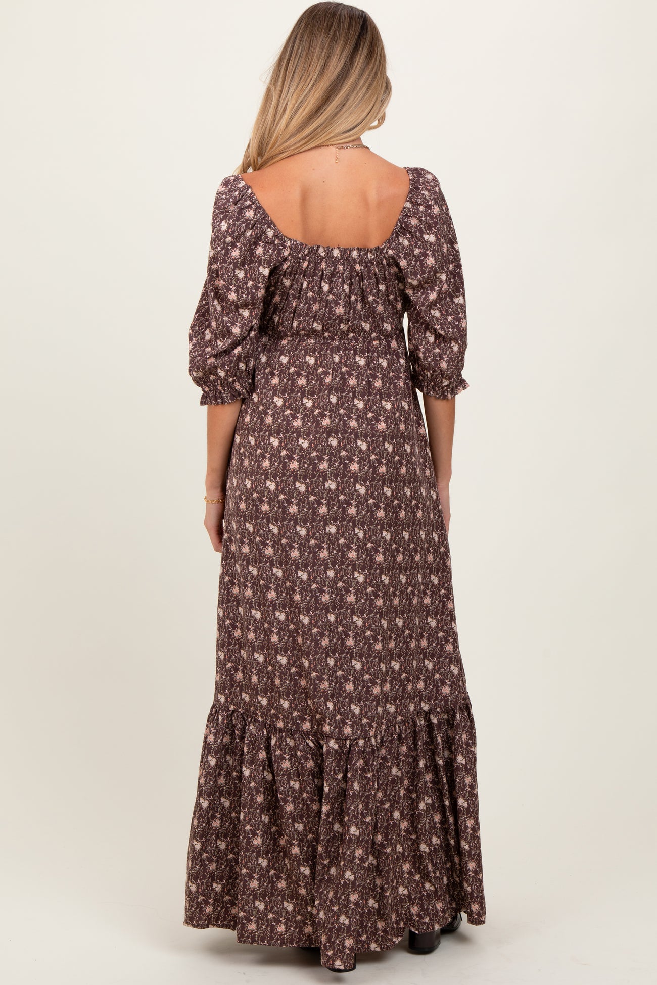 woman wearing a brown floral maternity maxi dress with puff sleeves and a tiered ruffled hem, showing her back