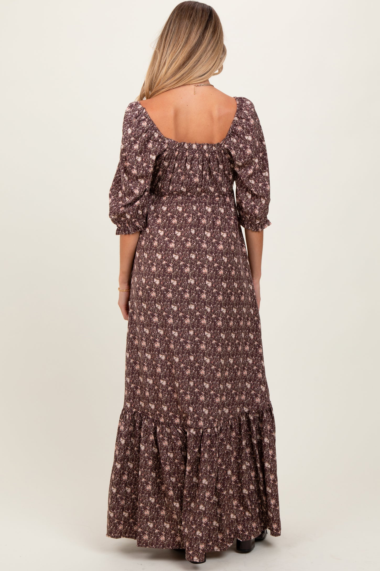 woman wearing a brown floral maternity maxi dress with puff sleeves and a tiered ruffled hem, showing her back