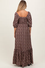 woman wearing a brown floral maternity maxi dress with puff sleeves and a tiered ruffled hem, showing her back