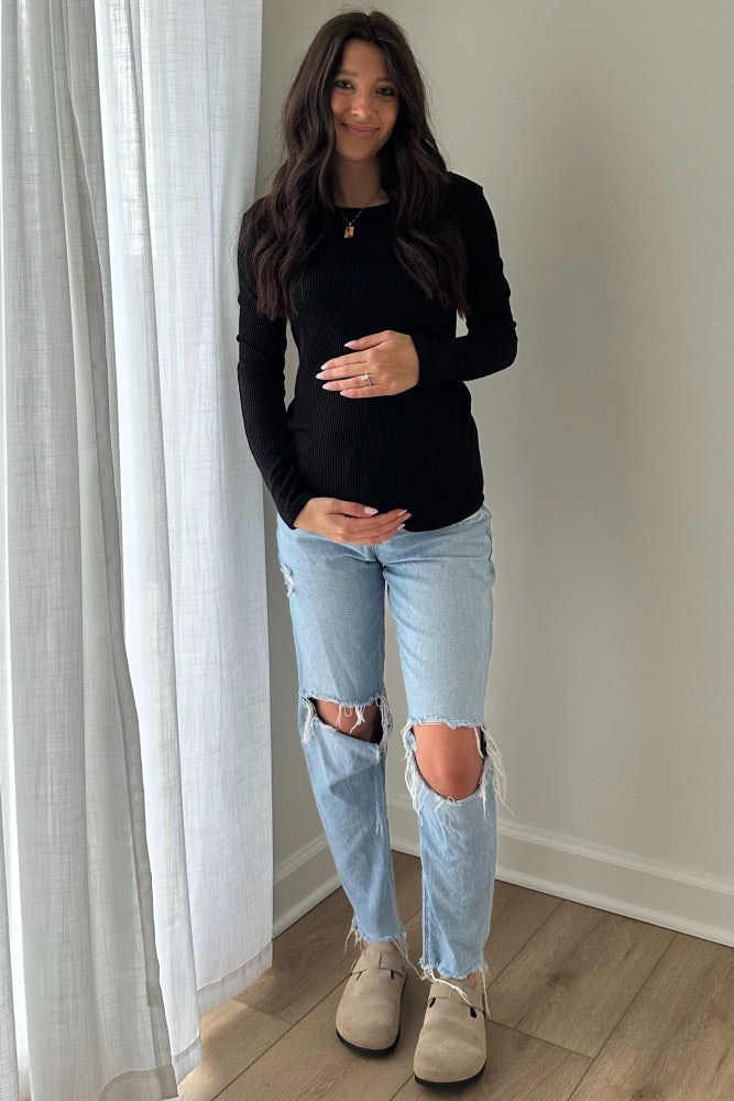 woman wearing a black long sleeve maternity top and light blue ripped jeans, holding her baby bump