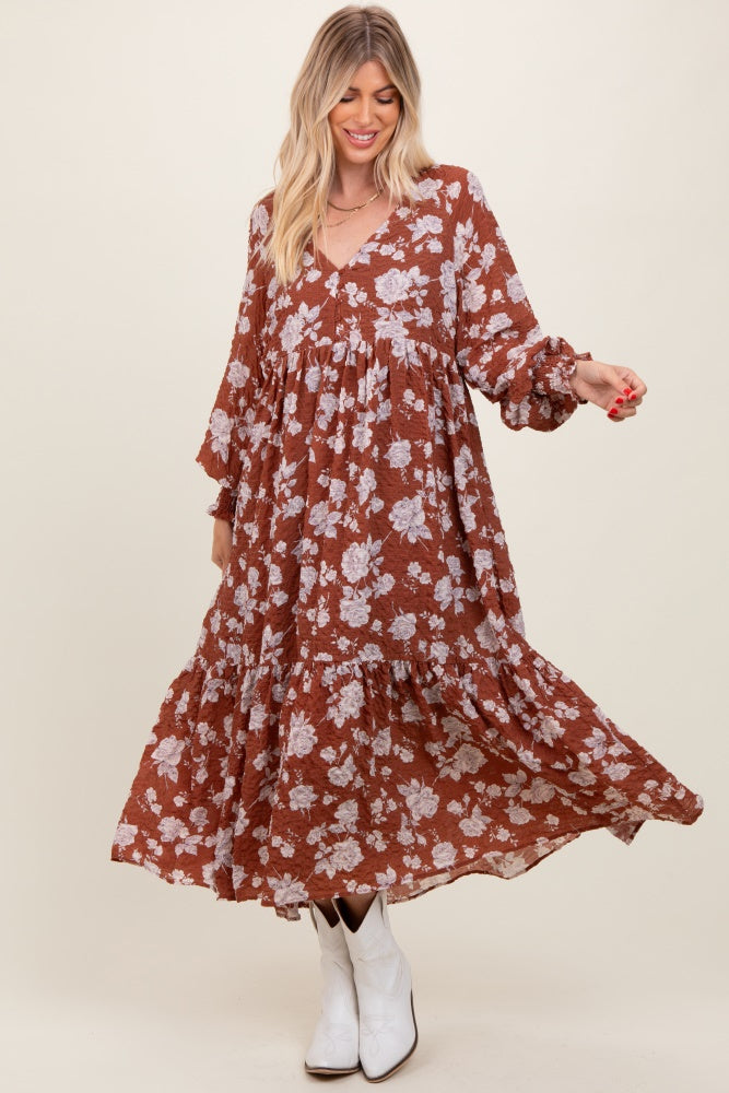 woman wearing a rust floral print maxi dress with long sleeves and a tiered skirt