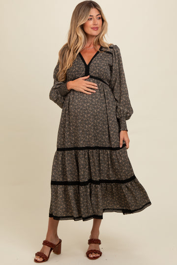 woman wearing a black floral maternity maxi dress with puff sleeves and a tiered skirt, holding her baby bump