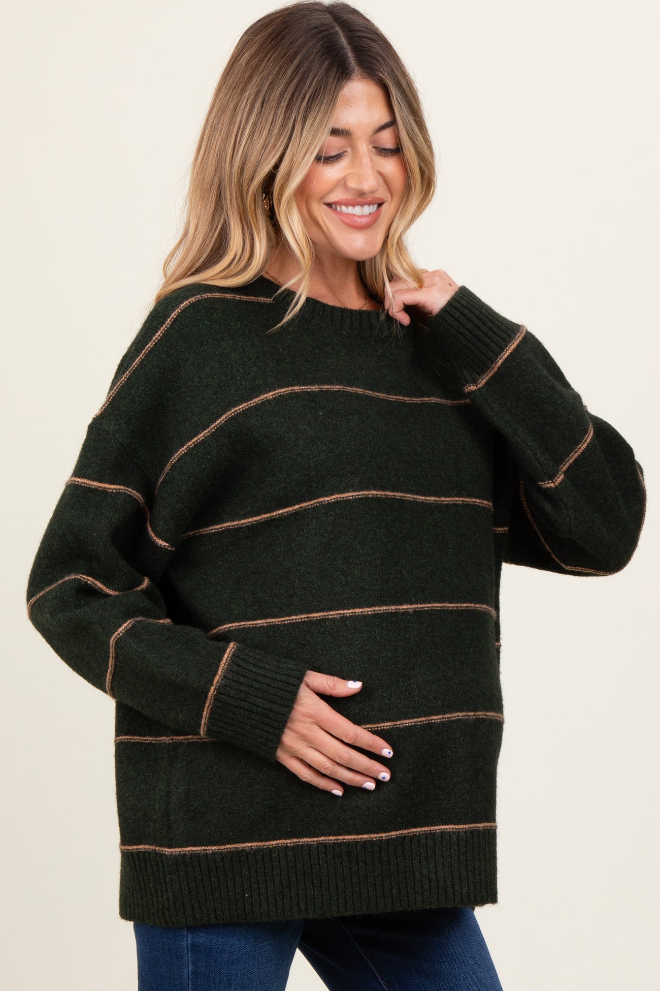 woman wearing a dark green striped maternity sweater and cradling her baby bump