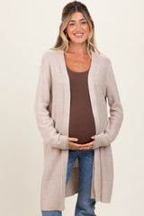 woman wearing a beige long cardigan over a brown tank top, showing her baby bump in maternity wear