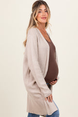 woman wearing a beige long cardigan and brown tank top, showcasing her baby bump in maternity wear