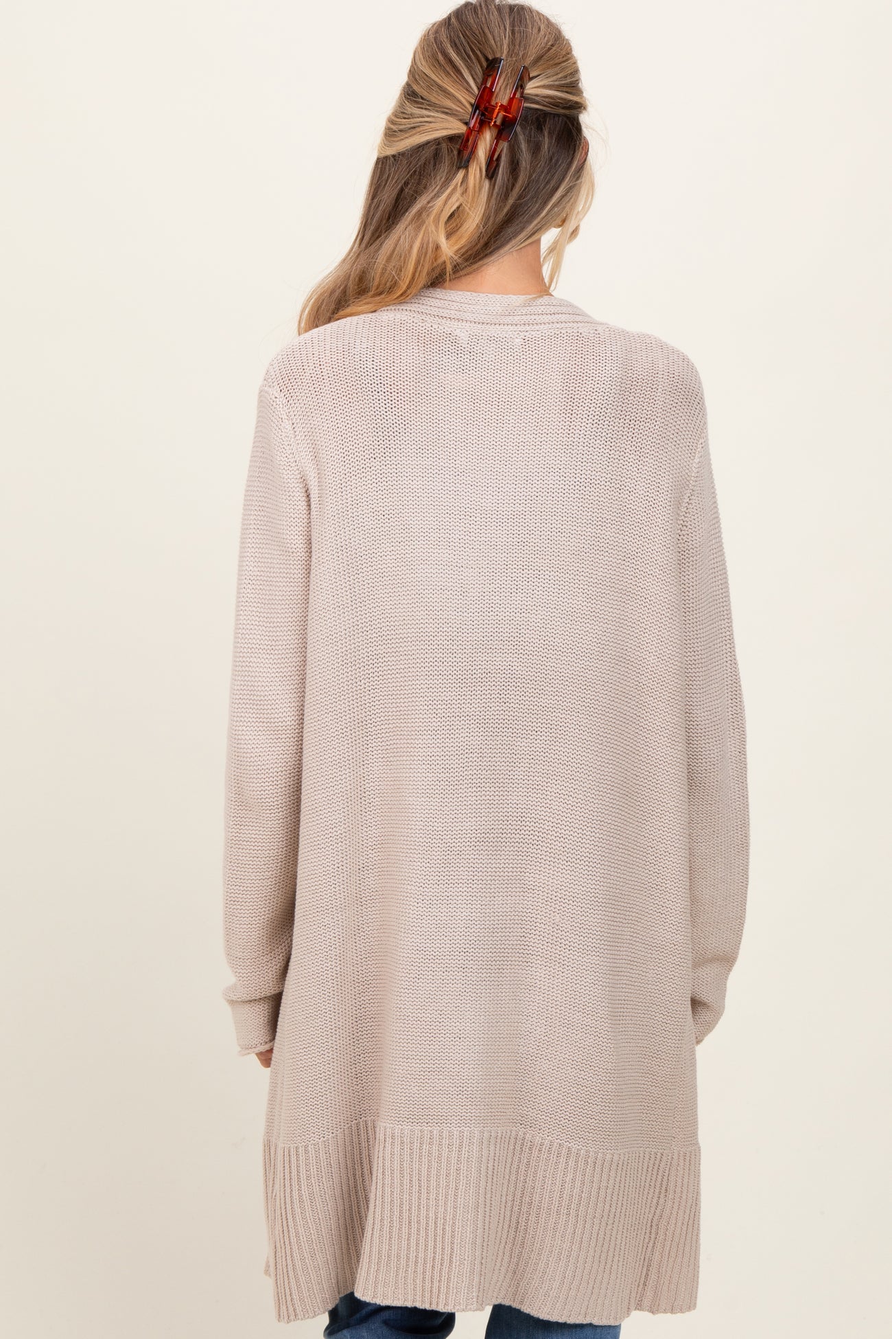 woman wearing a beige long knitted maternity cardigan, viewed from the back
