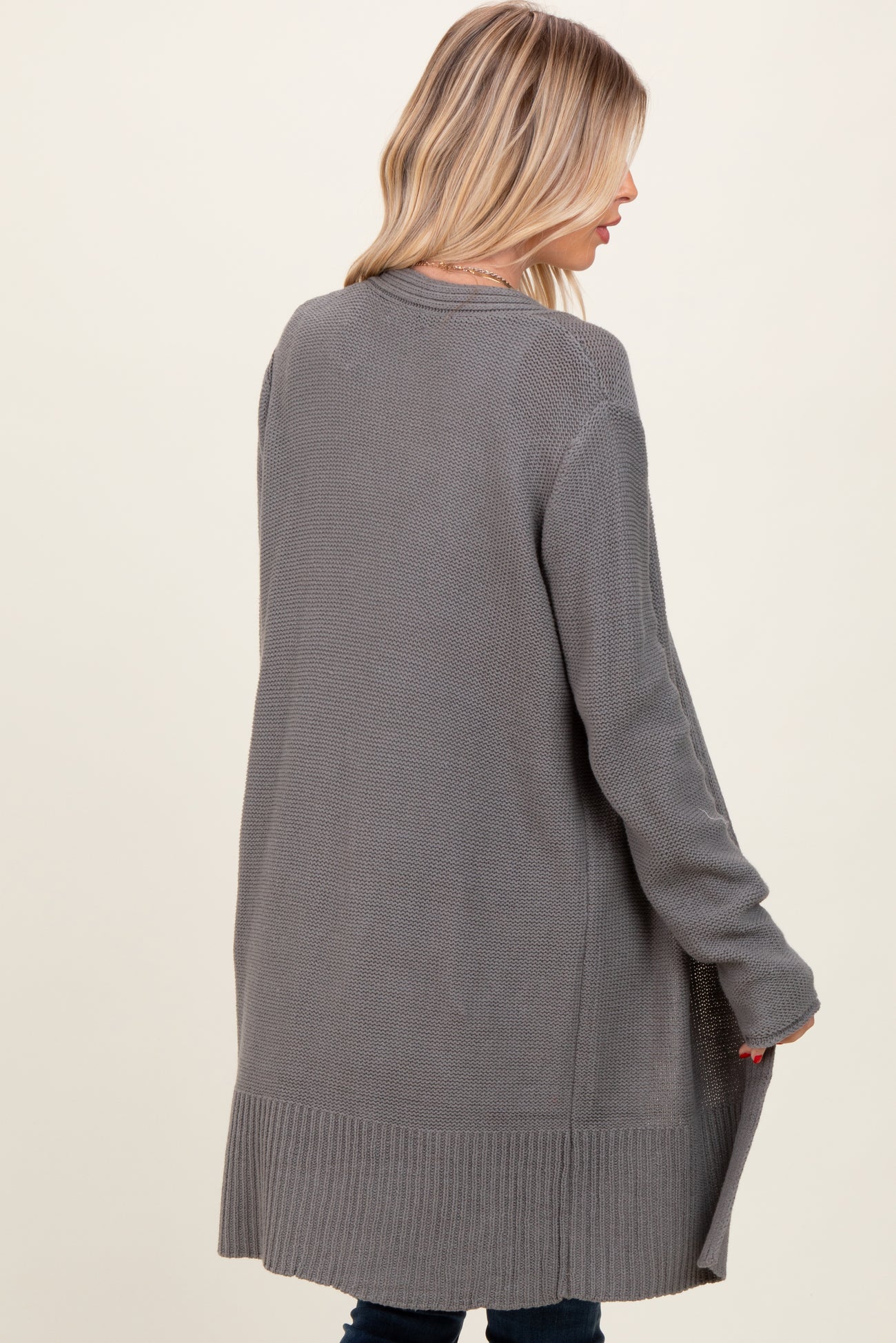 woman wearing a long gray knitted cardigan with ribbed detailing, shown from the back