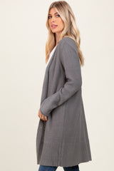 woman wearing a long gray cardigan with a textured finish and open front, styled with a white top and jeans