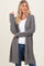 woman wearing a long grey knit cardigan over a white top and blue jeans