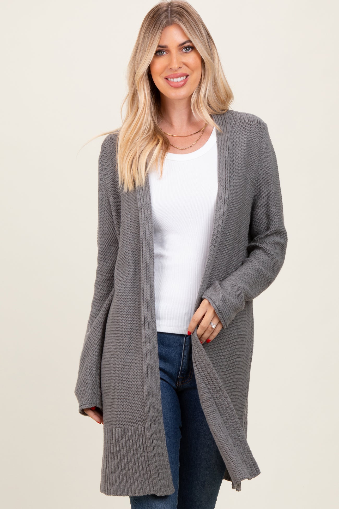 woman wearing a gray long cardigan over a white top and blue jeans, smiling at the camera