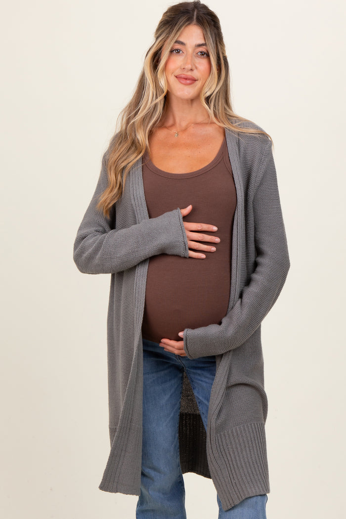woman wearing a gray long cardigan over a brown ribbed tank top and holding her baby bump