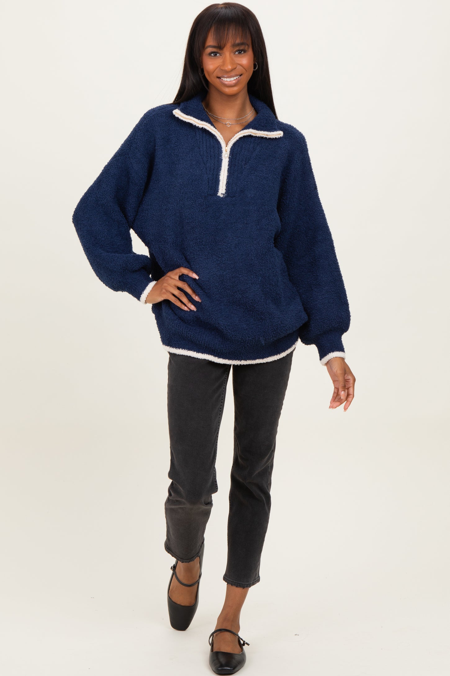 woman wearing a navy blue fuzzy pullover with a quarter zip and white trim, paired with black cropped jeans