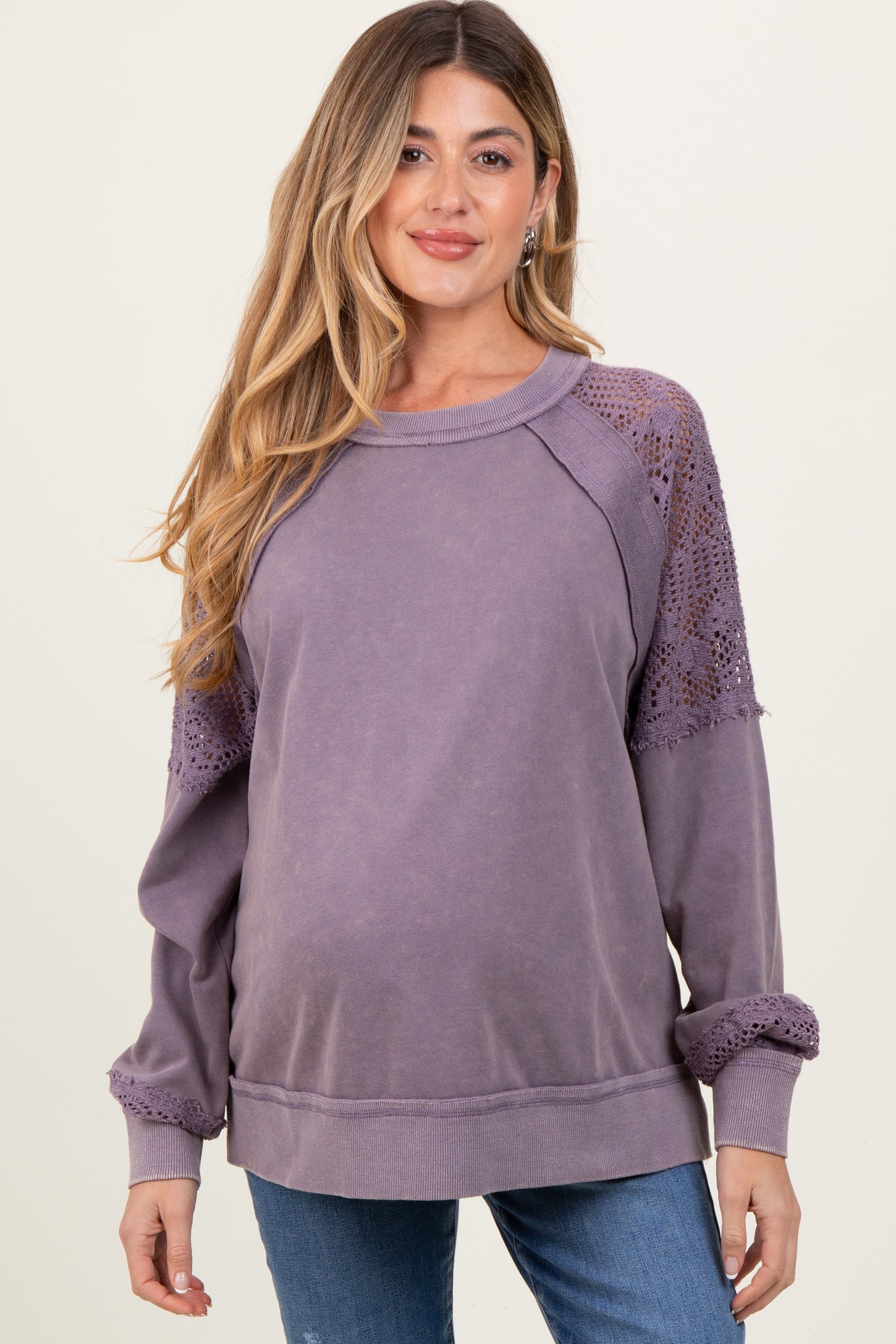 woman wearing a purple maternity sweatshirt with lace detail on sleeves and a visible baby bump