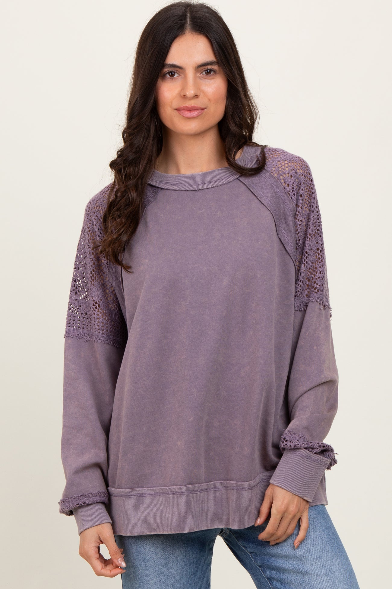 woman wearing a lavender oversized sweatshirt with lace details on the shoulders and ribbed cuffs, paired with blue jeans