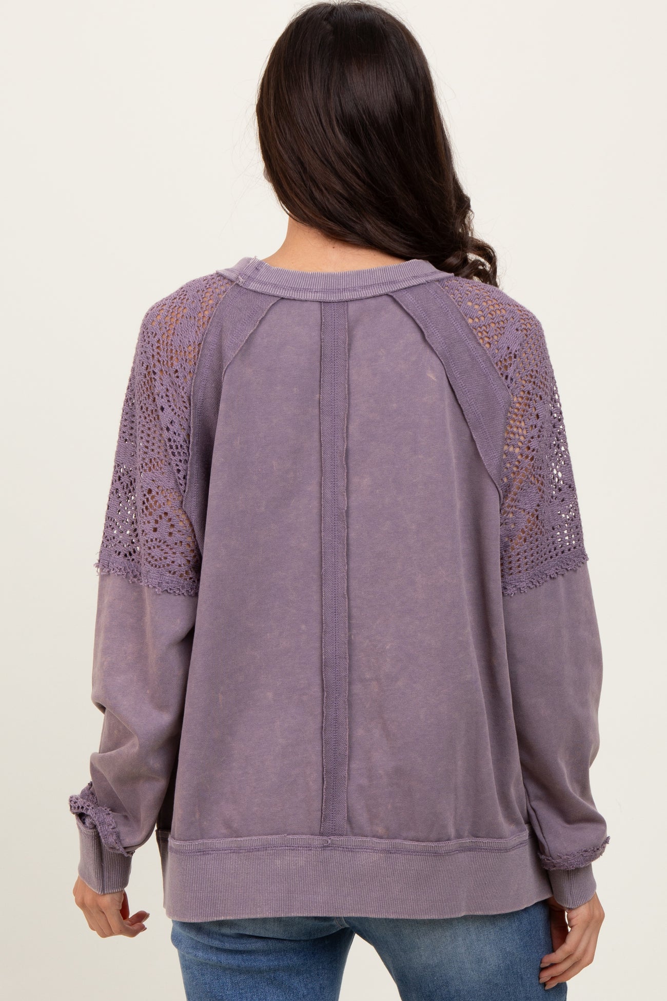 woman wearing a purple pullover sweatshirt with lace detailing on the shoulders and long sleeves, viewed from the back