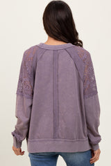woman wearing a purple pullover sweatshirt with lace detailing on the shoulders and long sleeves, viewed from the back