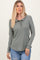 woman wearing a green ribbed long sleeve top with a ruffled collar and button placket, paired with denim shorts