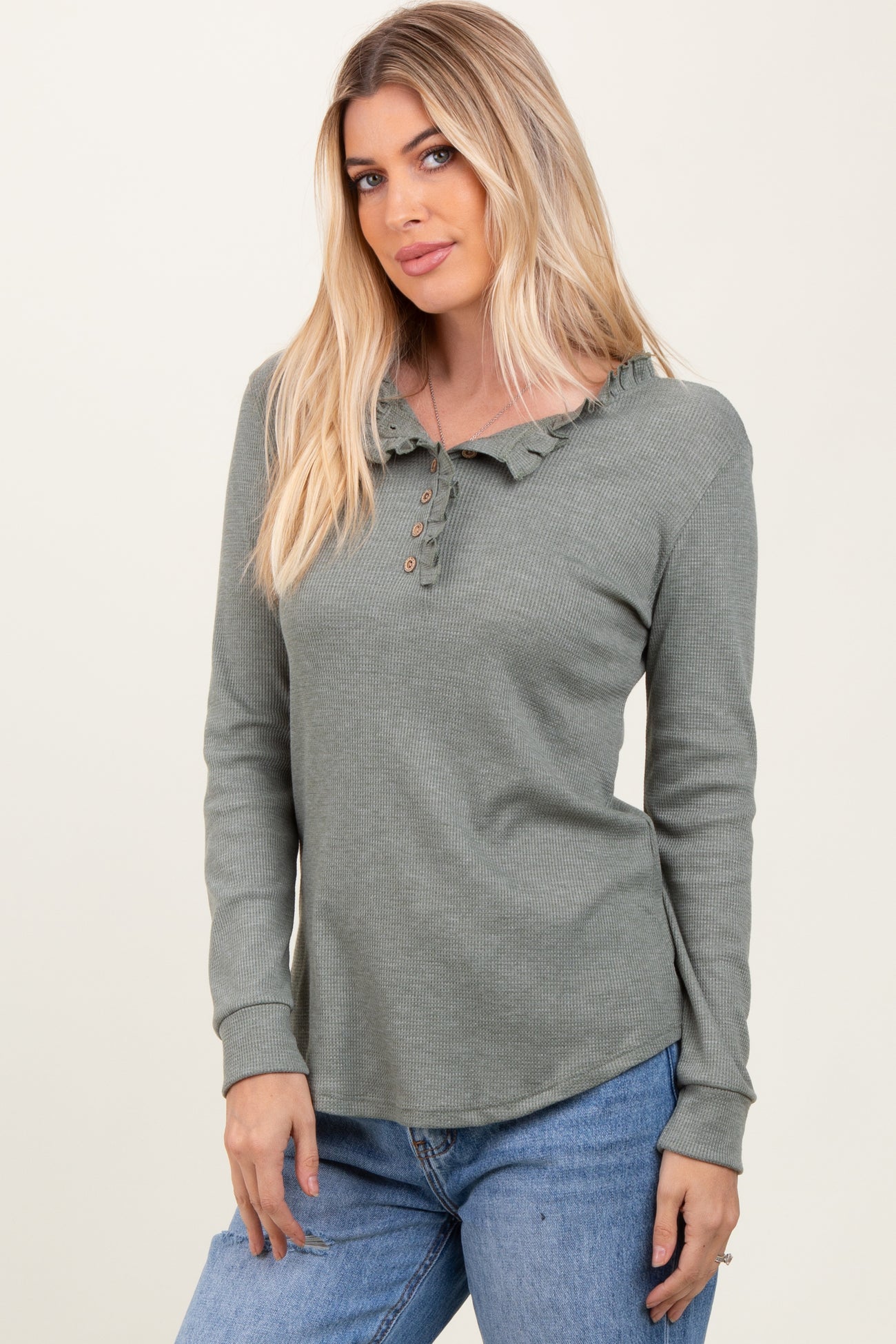 woman wearing a green ruffle collar long sleeve henley top with button details and paired with light blue jeans