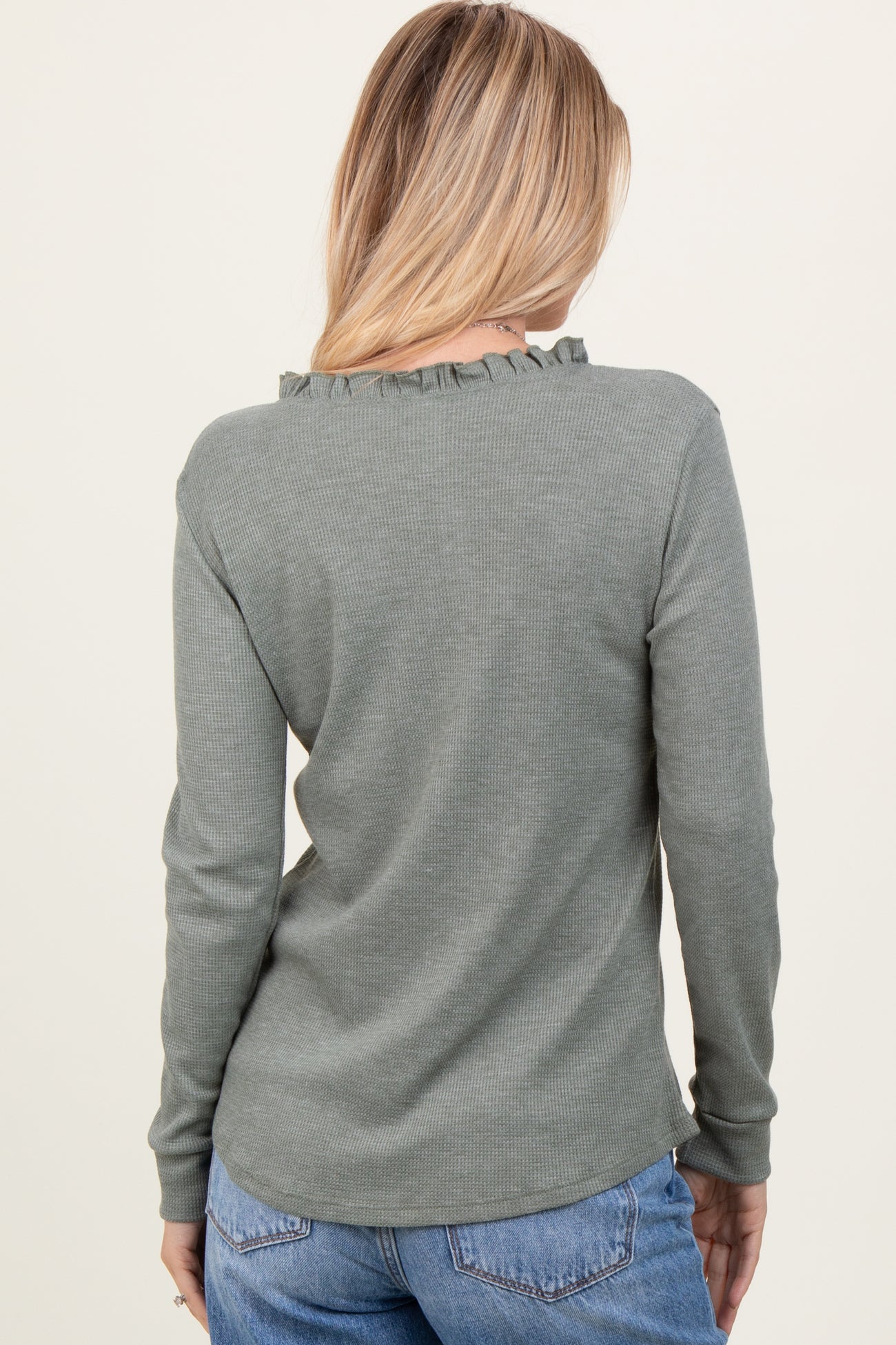 woman wearing a green long sleeve ribbed top with ruffle detail on the neckline, seen from the back