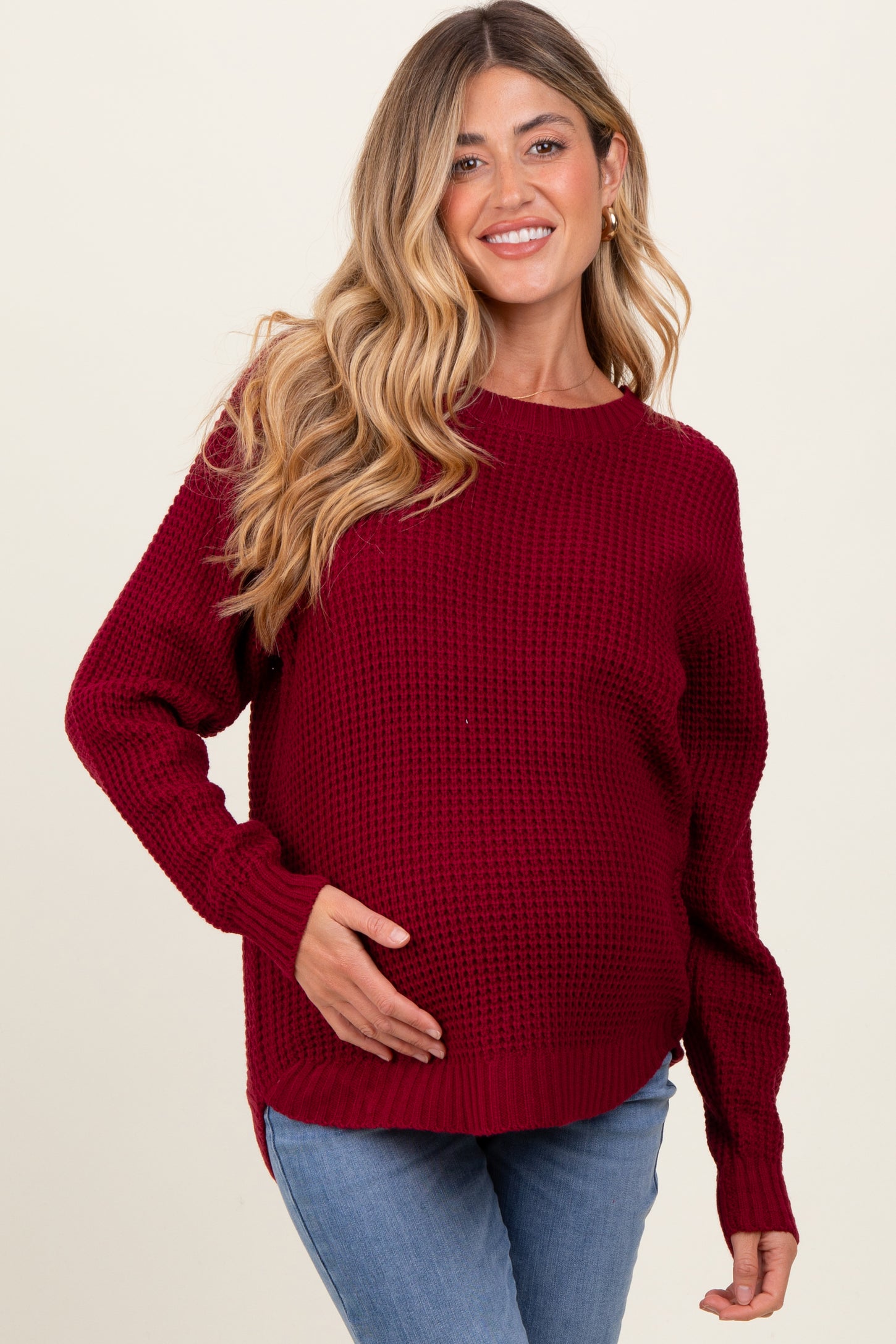 woman wearing a maroon knitted maternity sweater and holding her baby bump