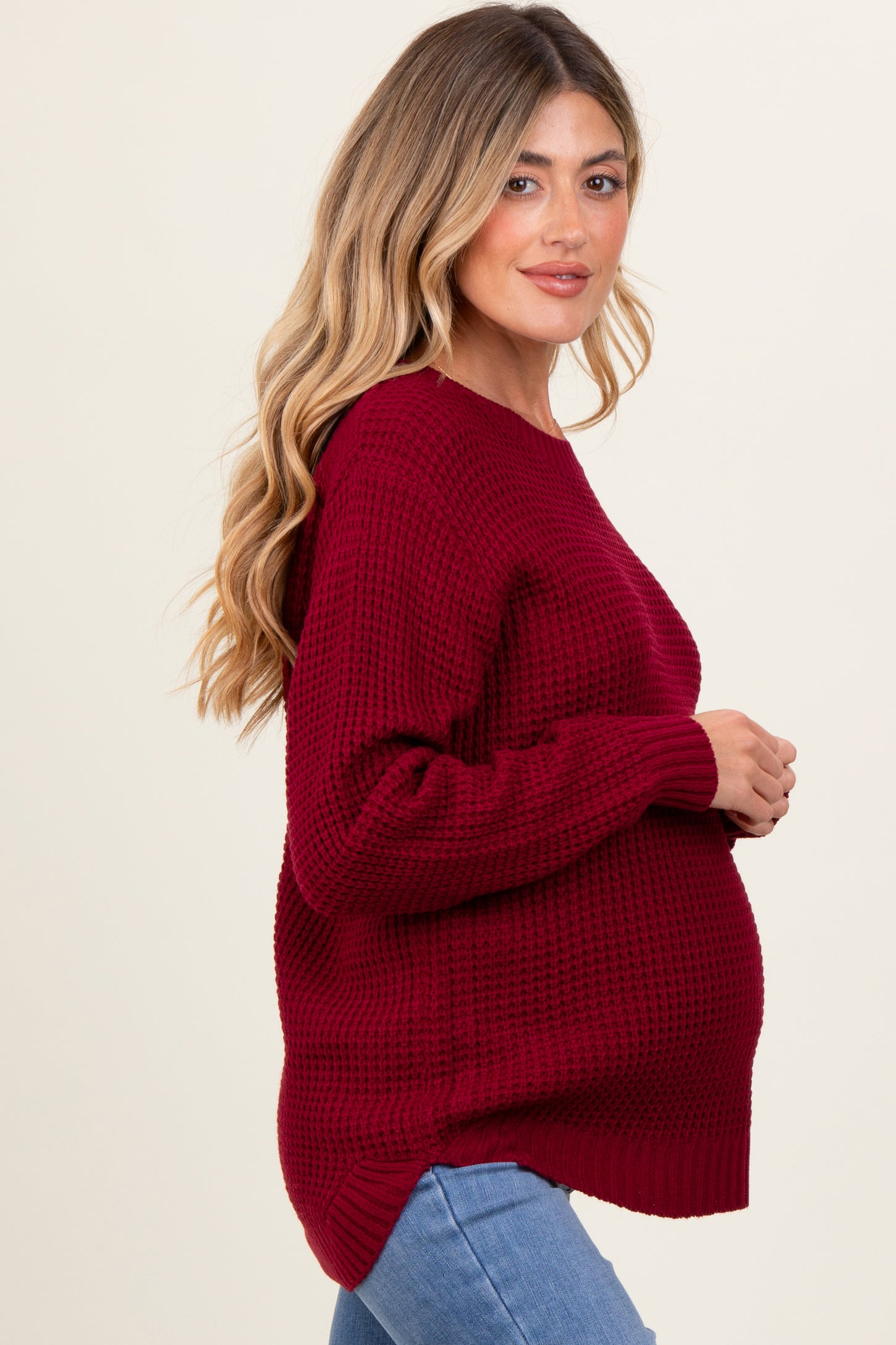 woman wearing a burgundy chunky knit maternity sweater with a side slit and visible baby bump