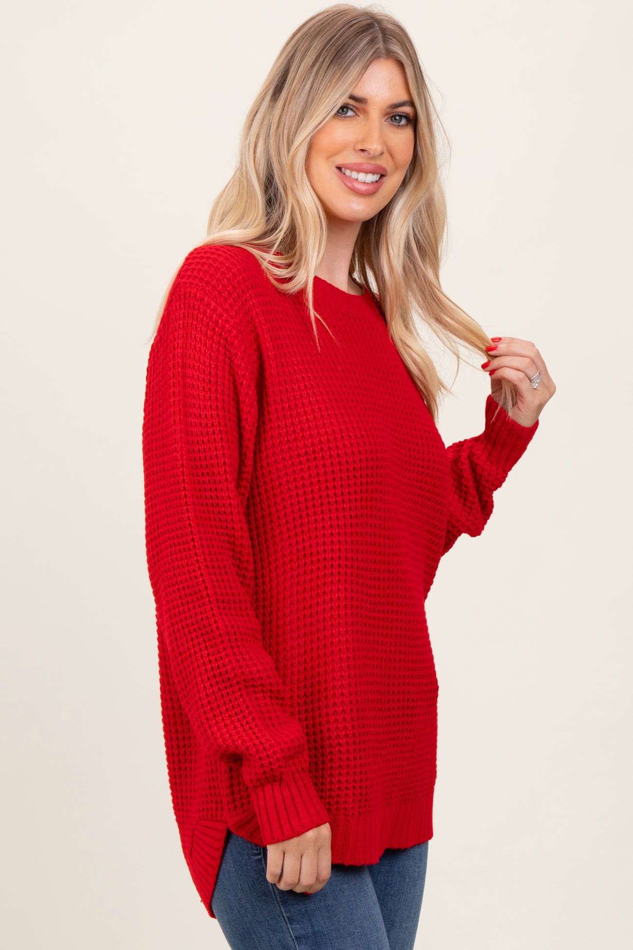 woman wearing a red oversized knit sweater with long sleeves and a side slit, smiling at the camera