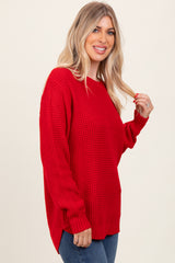 woman wearing a red oversized knit sweater with long sleeves and a side slit, smiling at the camera