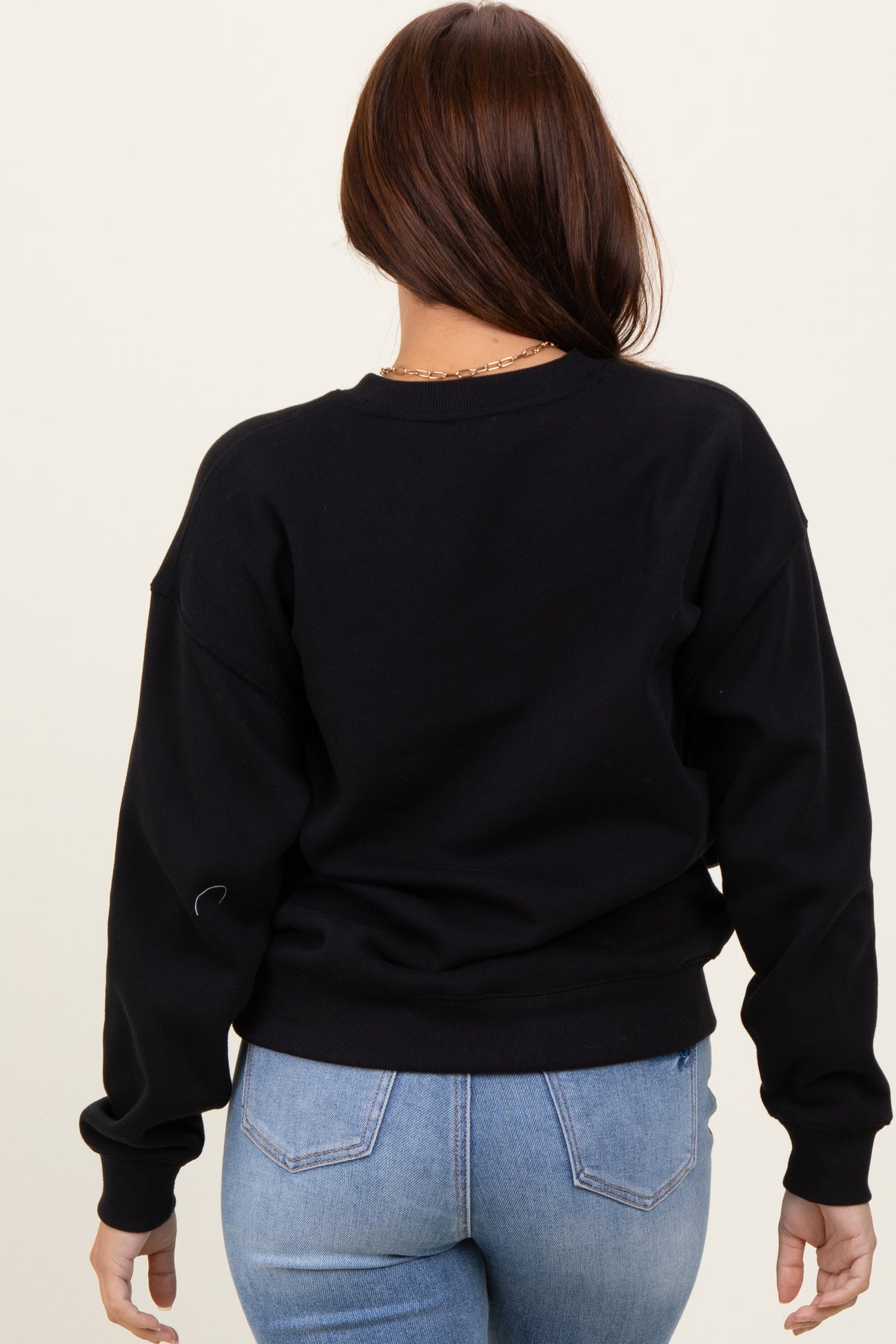 woman wearing a black oversized sweatshirt from the back with long sleeves and a relaxed fit paired with light blue jeans