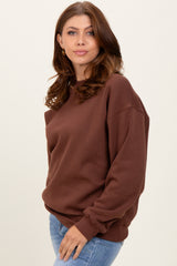 woman wearing a brown oversized sweatshirt with dropped shoulders and ribbed cuffs, styled with blue jeans