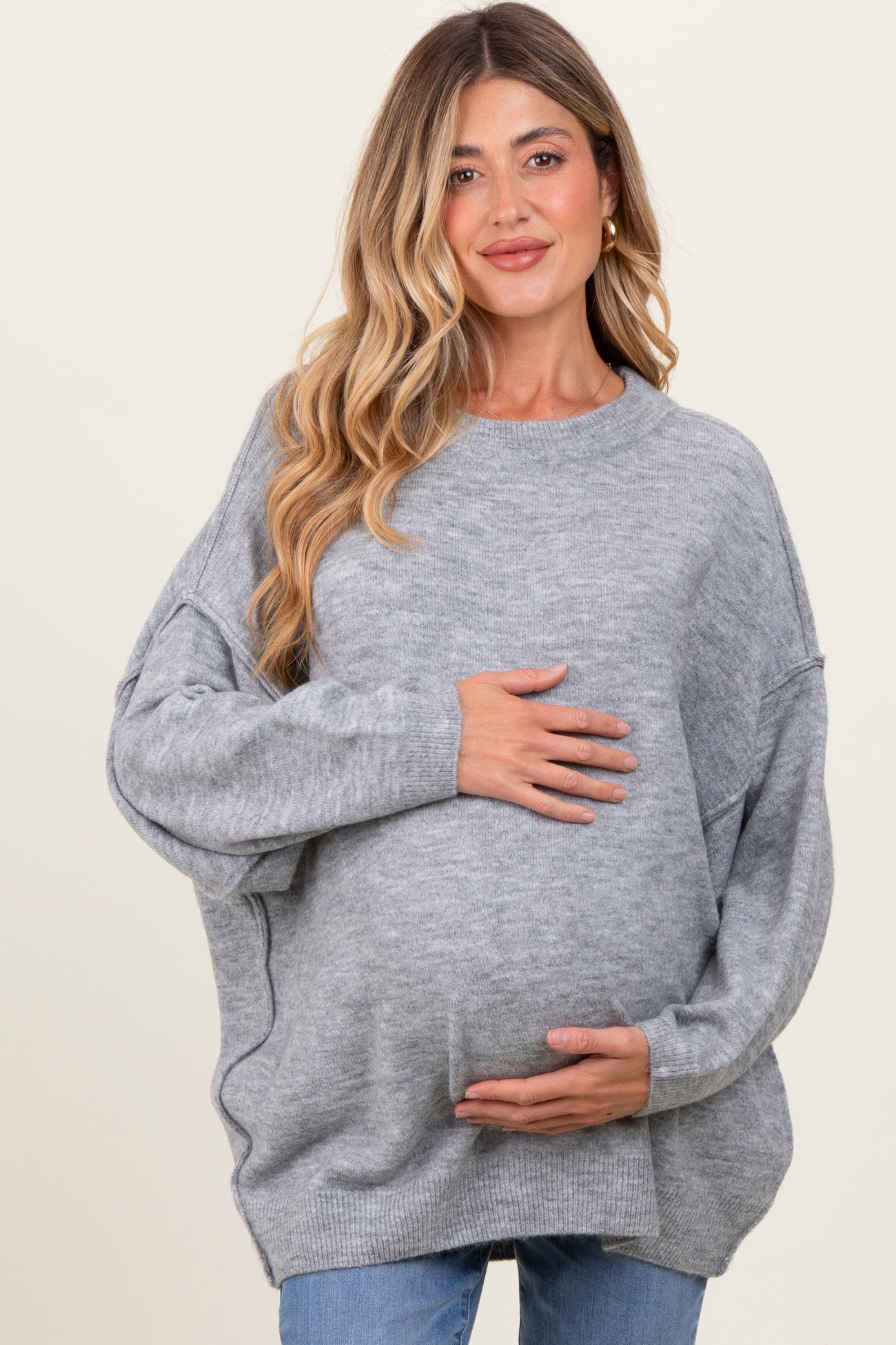 woman wearing a gray oversized maternity sweater and holding her baby bump
