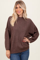 woman wearing a brown oversized knit sweater with dropped shoulders and long sleeves paired with blue jeans