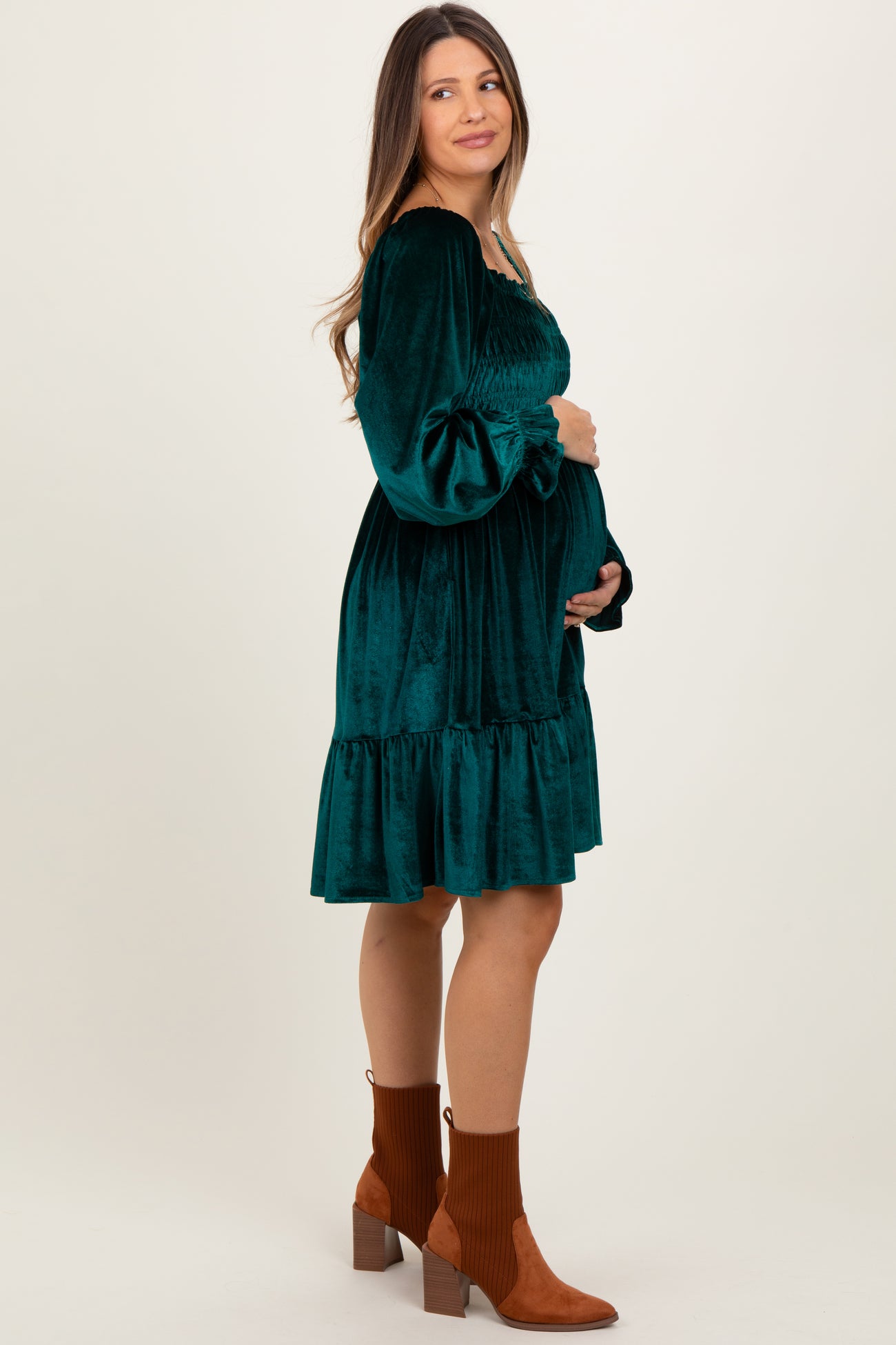 woman wearing a green velvet maternity dress with puff sleeves and a ruffled hem, holding her baby bump