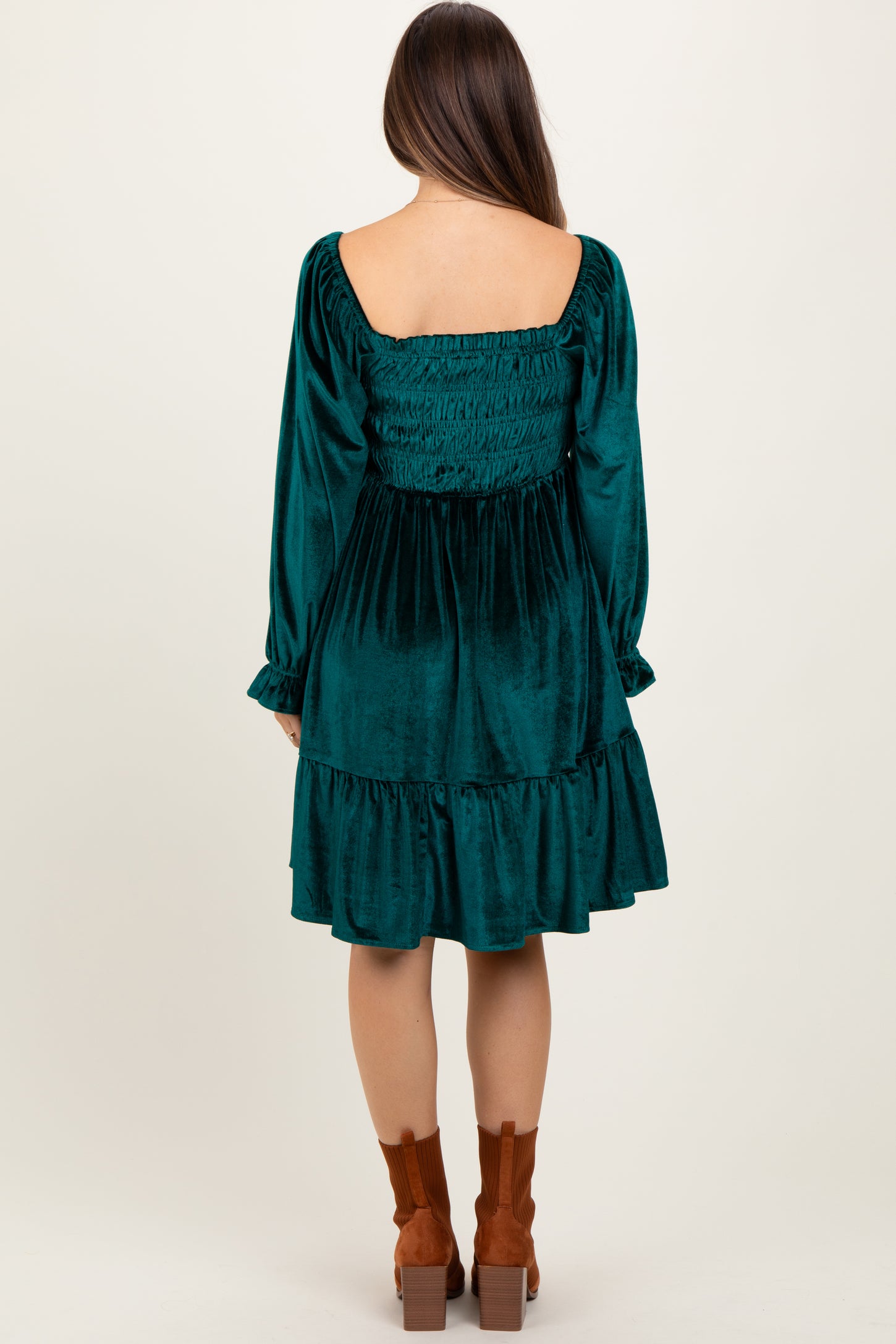 woman wearing a teal velvet maternity dress with a smocked bodice and long sleeves, showing the back view