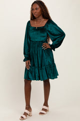 woman wearing a teal smocked mini dress with long sleeves and a ruffled hem, standing on a neutral background