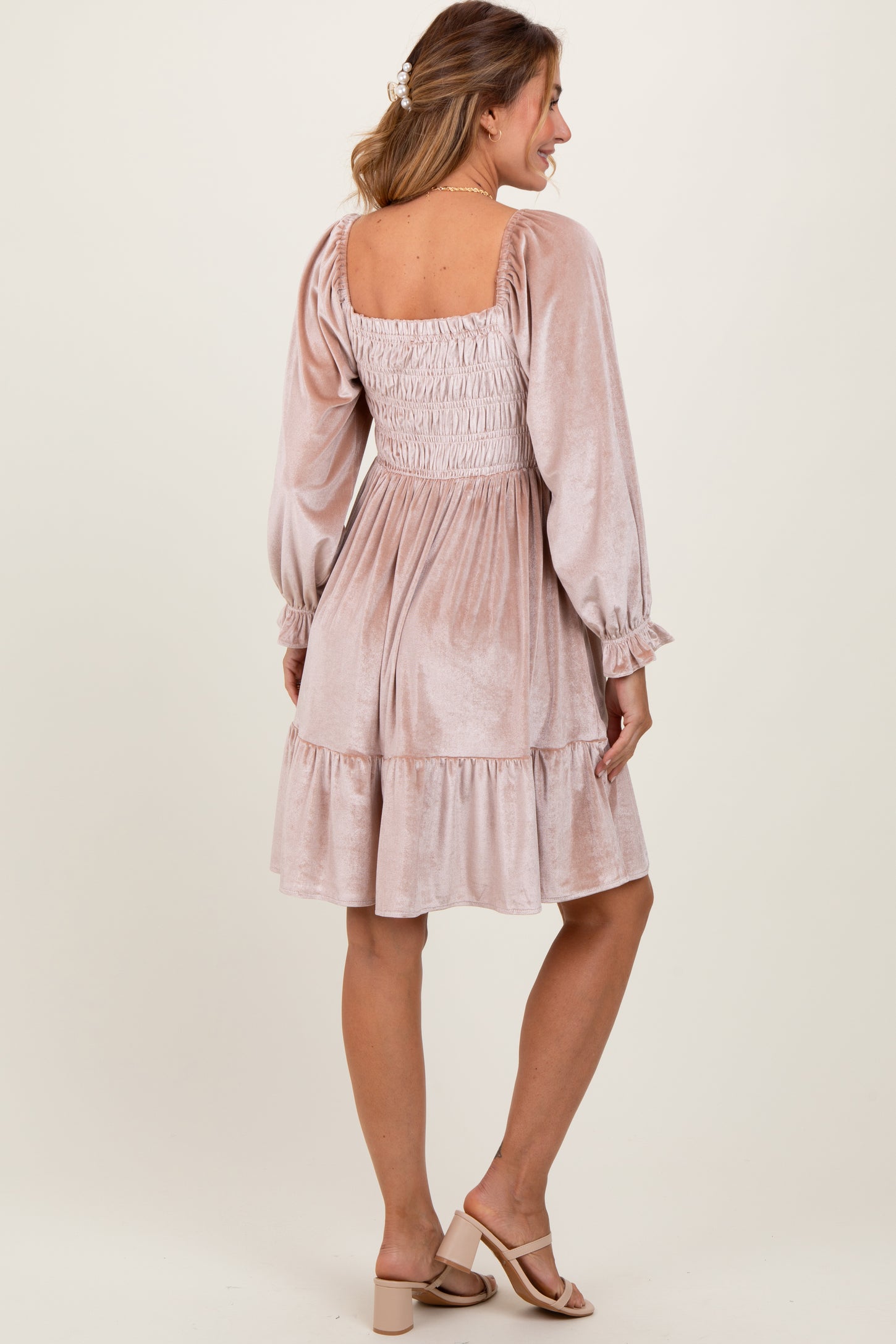 woman wearing a blush velvet smocked dress with long sleeves and a tiered hem, standing with her back towards the camera
