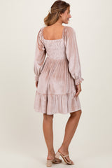 woman wearing a blush velvet smocked dress with long sleeves and a tiered hem, standing with her back towards the camera