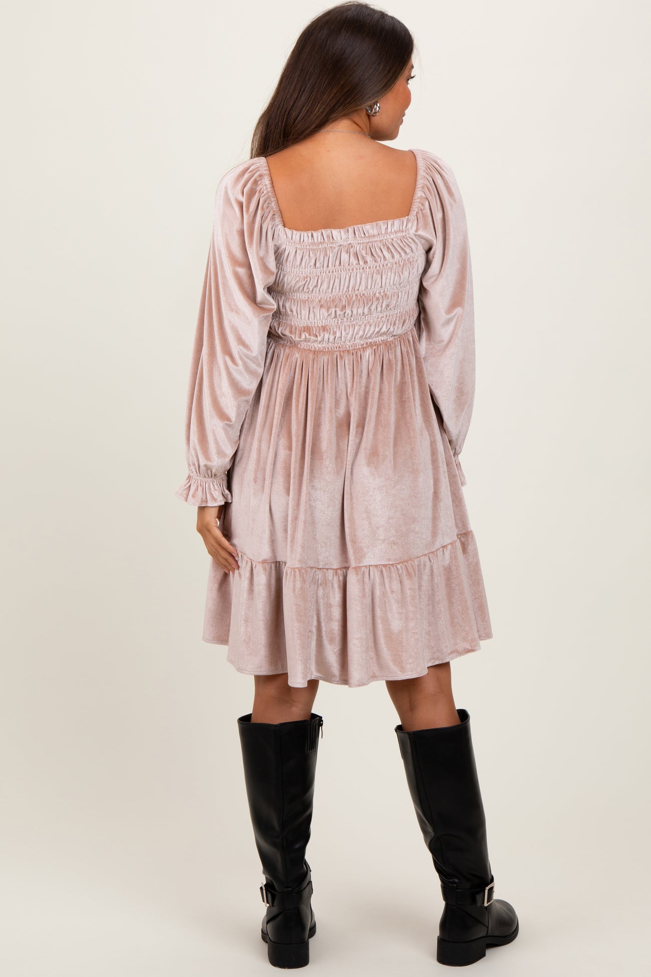 woman wearing a blush pink maternity dress with smocked bodice and long sleeves, standing with her back to the camera