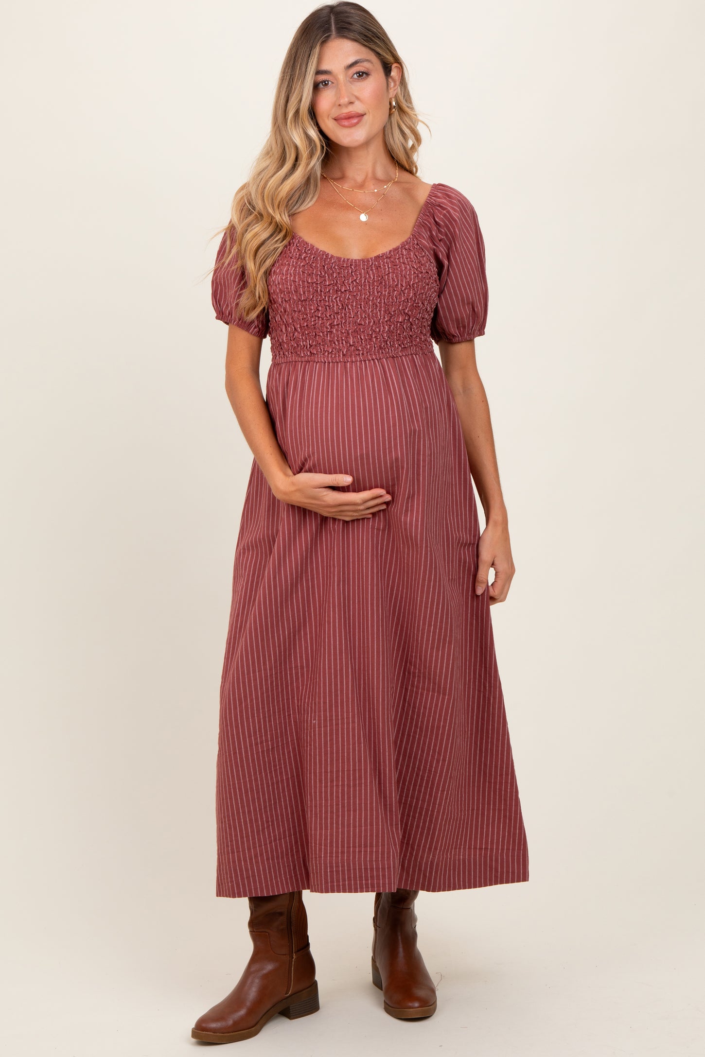 woman wearing a maroon striped maternity dress with short puff sleeves and a smocked bodice, holding her baby bump