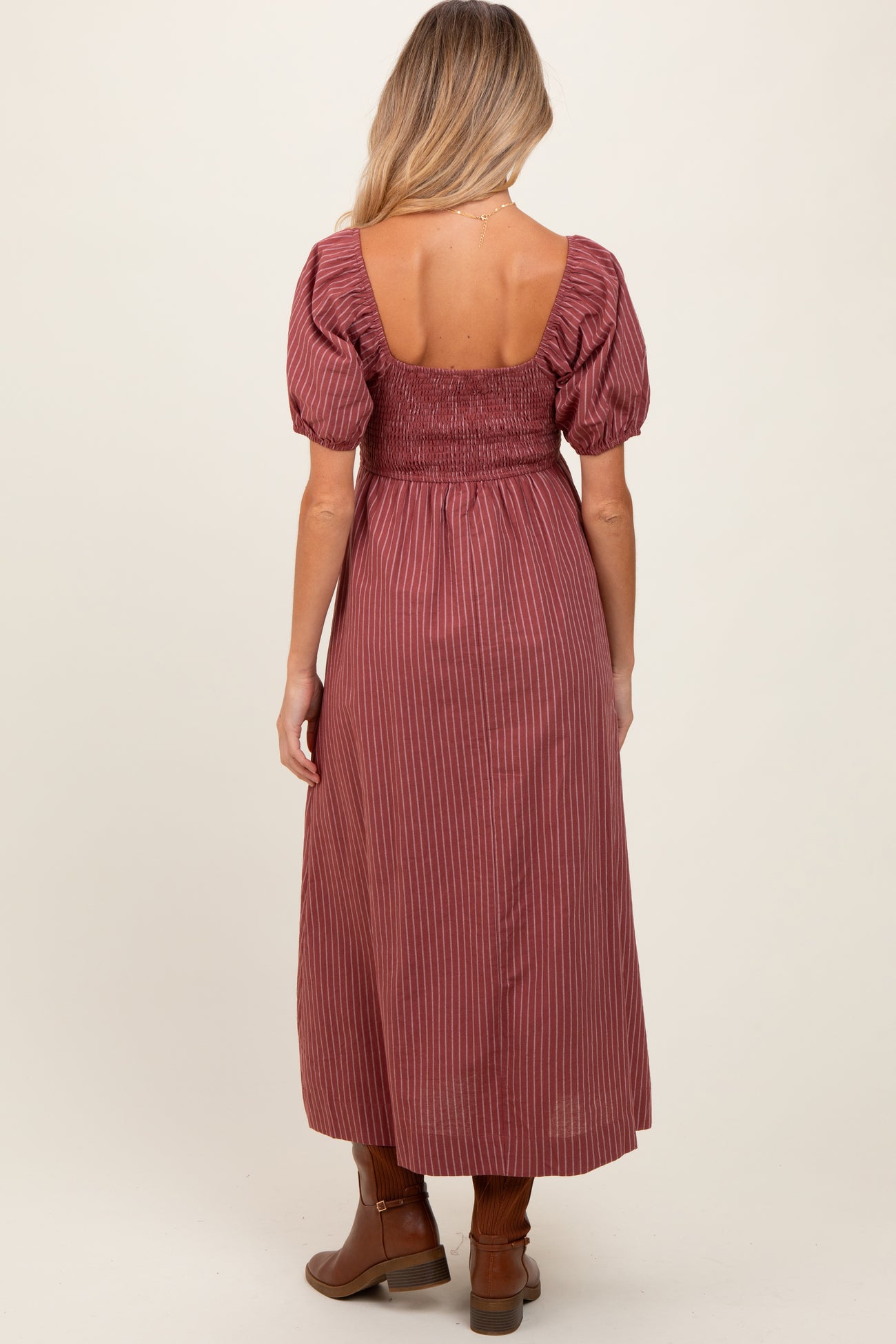 woman wearing a burgundy striped maternity dress with puff sleeves and a smocked back, standing sideways