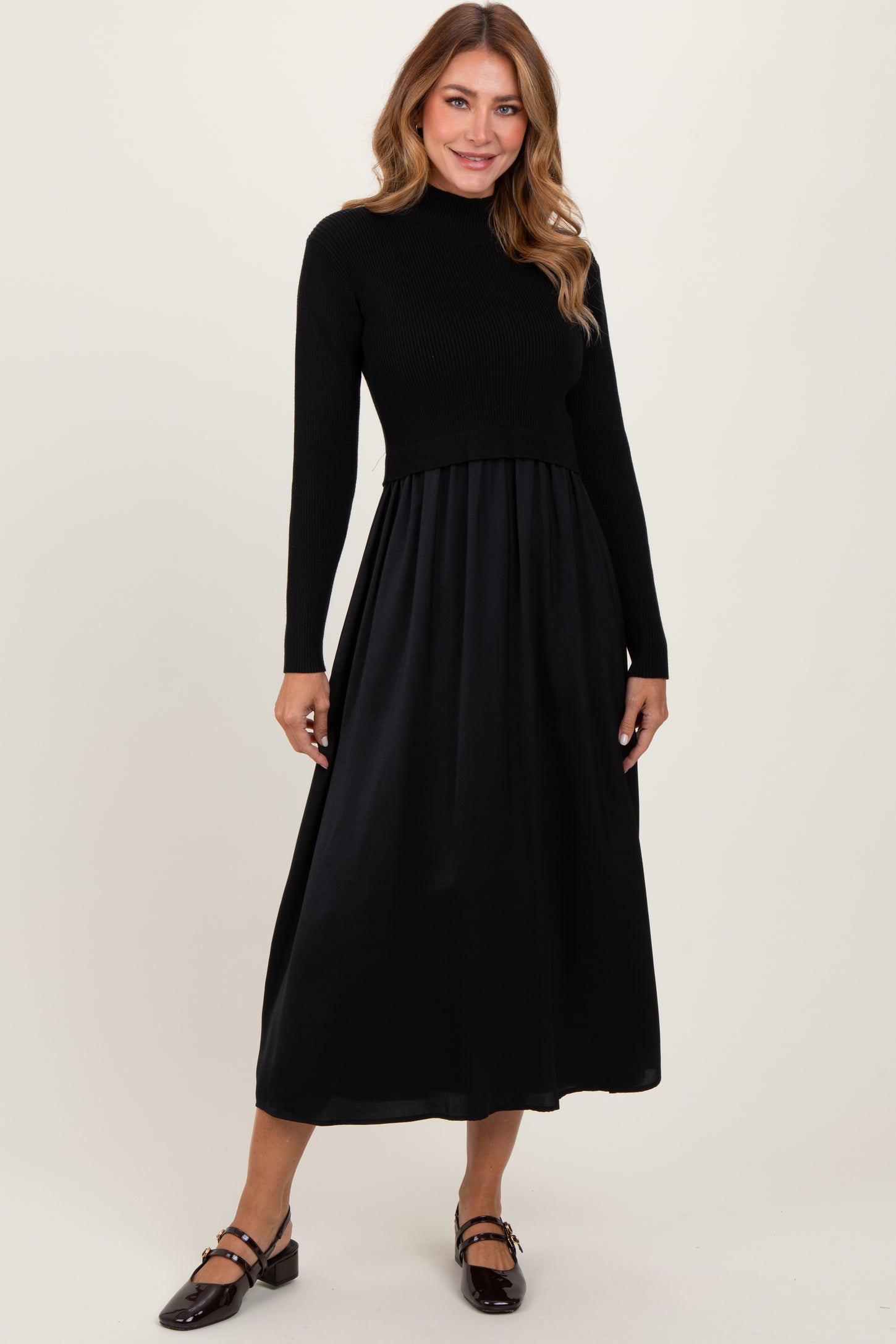 woman wearing a black long sleeve ribbed top and a flowy black midi dress with a fitted waist