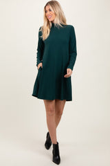 woman wearing a dark green long sleeve swing dress with pockets and ankle boots