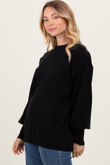 woman wearing a black oversized sweater with puff sleeves and a rounded neckline, paired with blue jeans