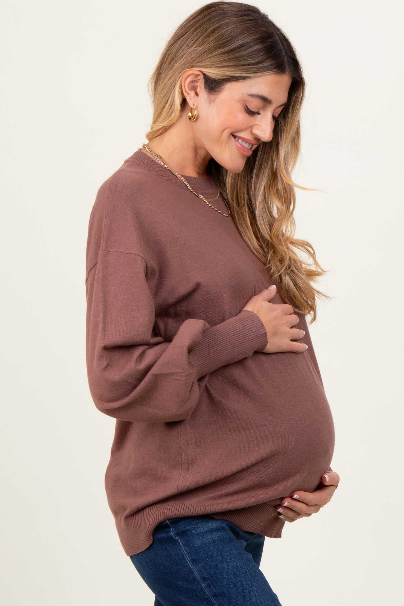 woman wearing a brown oversized maternity sweater and holding her baby bump