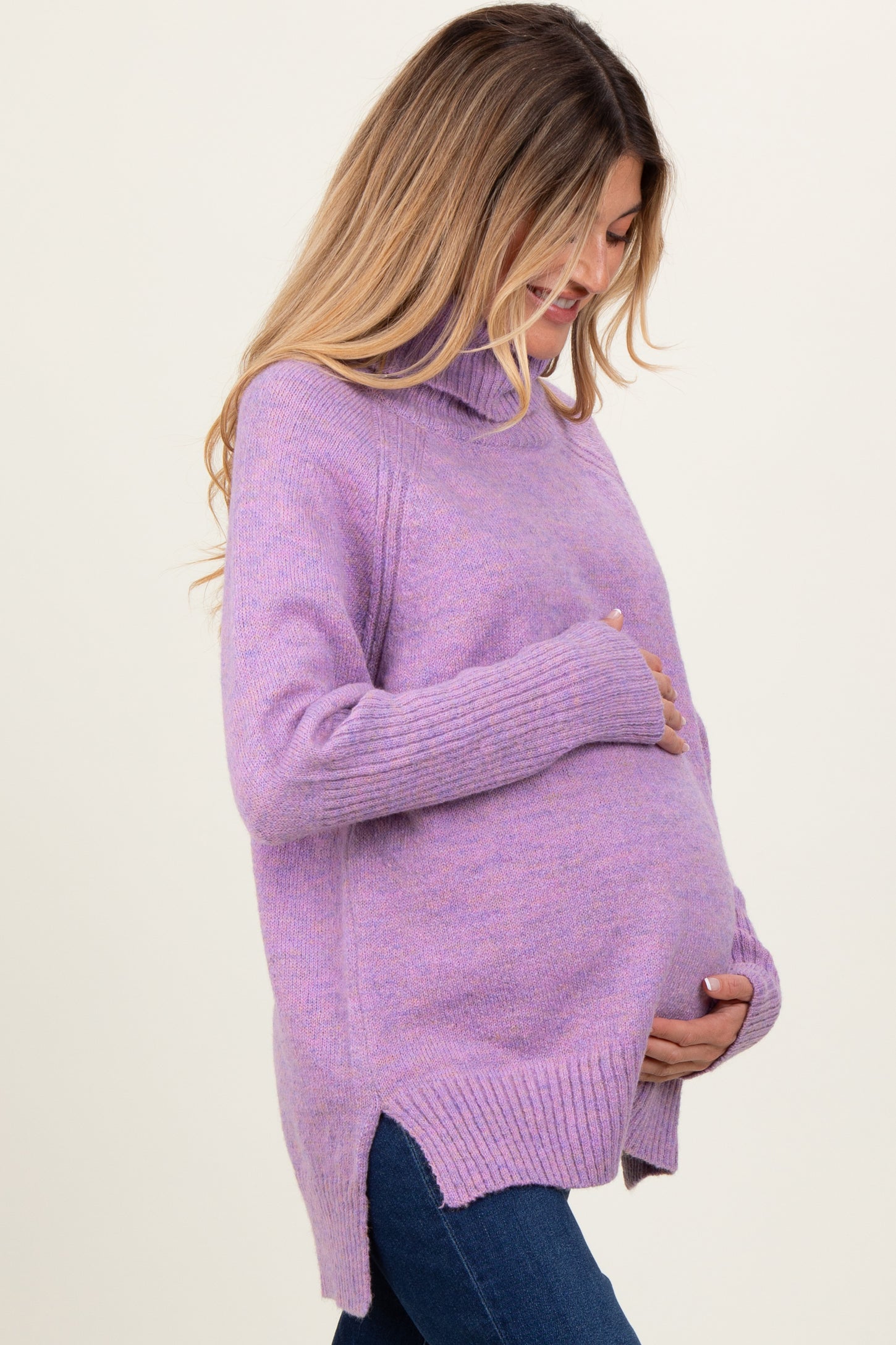 woman wearing a lavender maternity turtleneck sweater and holding her baby bump