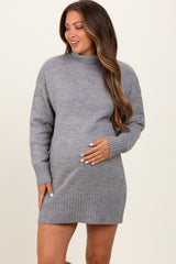 woman wearing a gray maternity sweater dress with a high neck and ribbed hem, gently cradling her baby bump