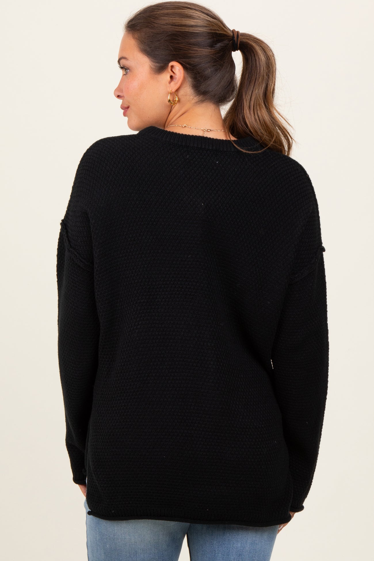 woman wearing a black oversized maternity sweater with long sleeves, viewed from the back